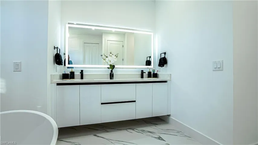 Full bathroom with light marble finish floors, double vanity, and a soaking tub