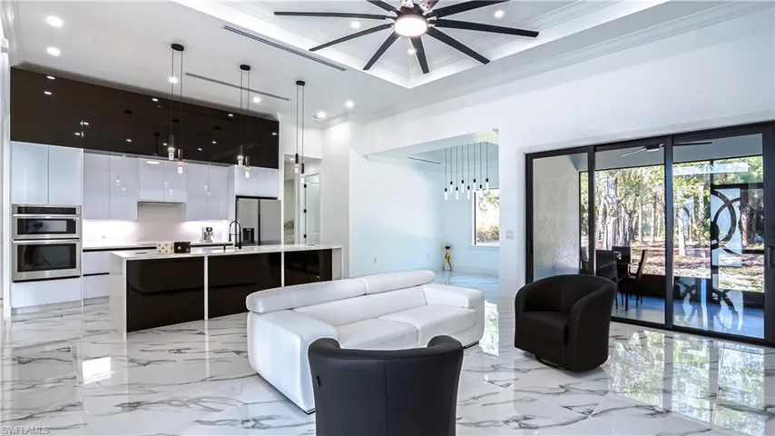 Living area featuring light marble finish flooring, recessed lighting, a ceiling fan, a high ceiling, and ornamental molding
