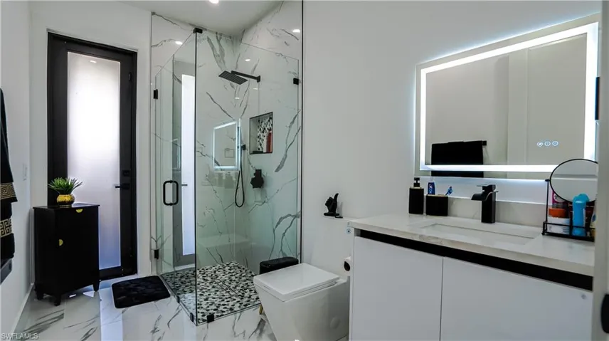 Full bath featuring vanity, a marble finish shower, light marble finish floors, and recessed lighting