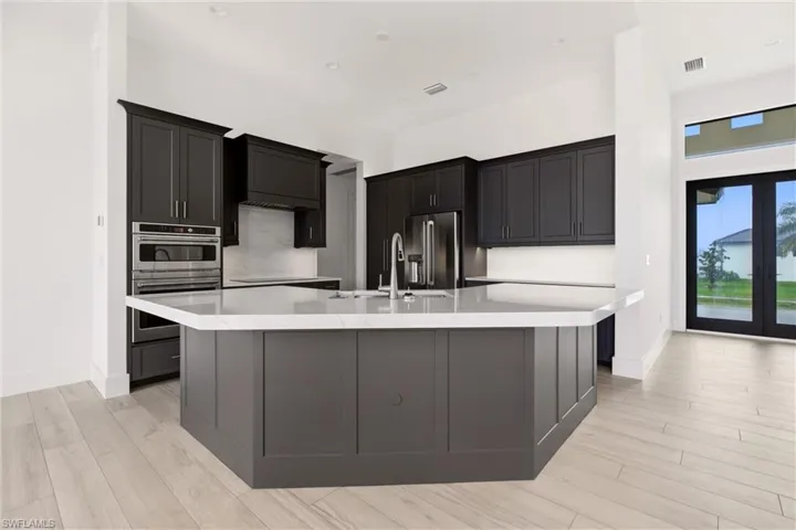 Kitchen with a spacious island, light tile finished floors, dark cabinets, and stainless steel appliances