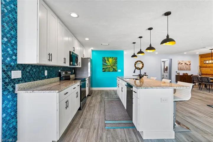 Kitchen with appliances with stainless steel finishes, hanging light fixtures, white cabinets, and an island with sink