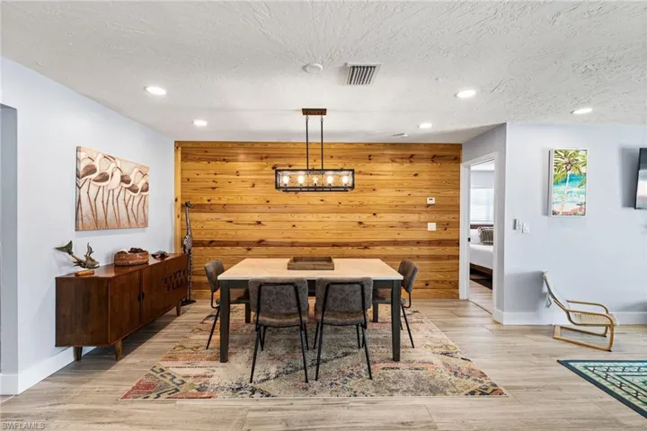 Kitchen featuring decorative light fixtures, white cabinetry, sink, a center island with sink, and wood walls