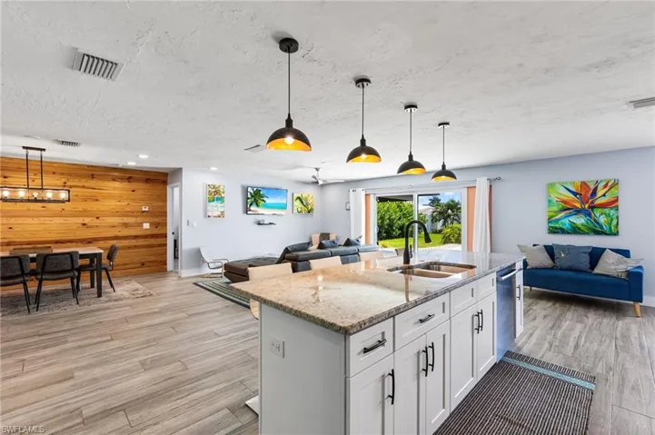 Kitchen featuring decorative light fixtures, white cabinetry, sink, a center island with sink, and wood walls