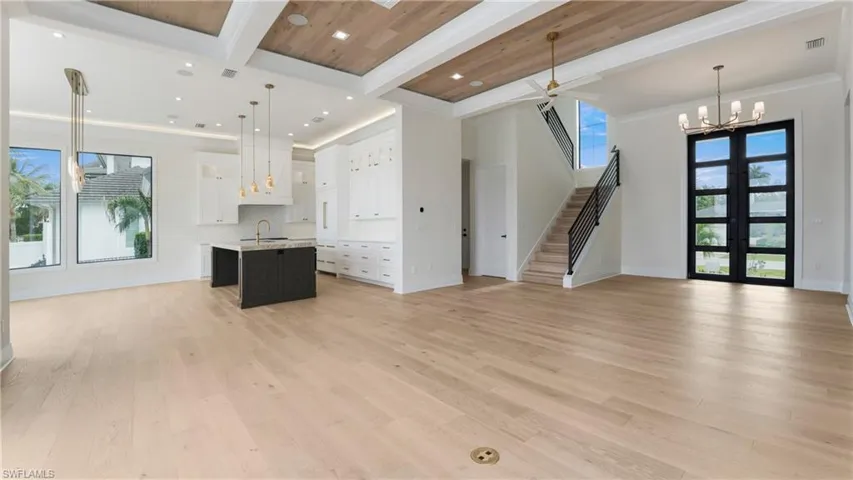 Unfurnished living room with beamed ceiling, light wood-type flooring, a chandelier, french doors, and a ceiling fan