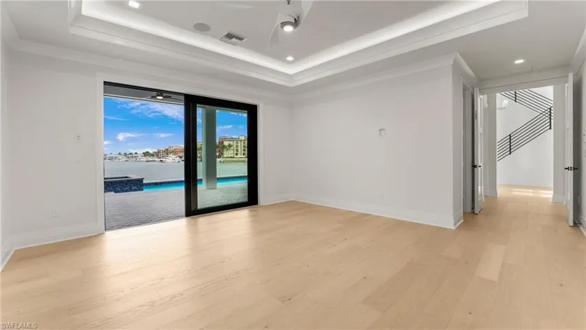 Spare room featuring light wood-type flooring, a ceiling fan, a raised ceiling, a water view, and recessed lighting