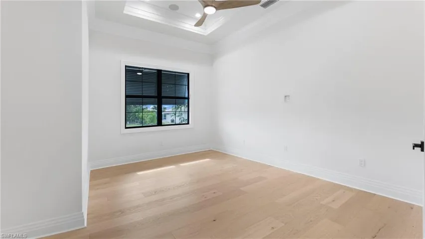 Unfurnished room with light wood-style flooring, a raised ceiling, ceiling fan, and crown molding
