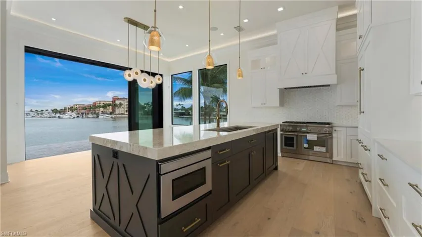 Kitchen featuring white cabinetry, stainless steel appliances, decorative light fixtures, backsplash, and light wood-type flooring