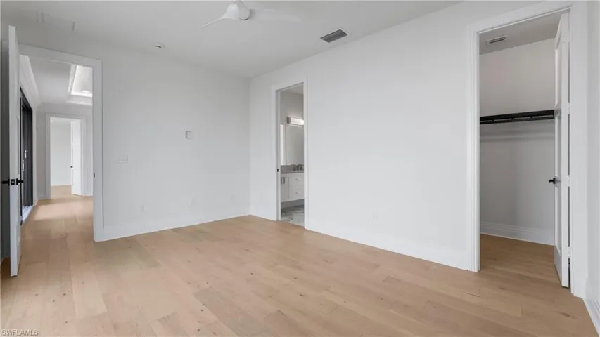 Unfurnished bedroom with a spacious closet, light wood-style flooring, a ceiling fan, and ensuite bathroom