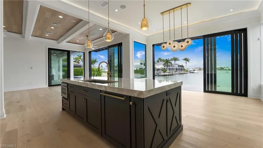 Kitchen featuring hanging light fixtures, light stone counters, a kitchen island with sink, light wood-style flooring, and dark cabinets