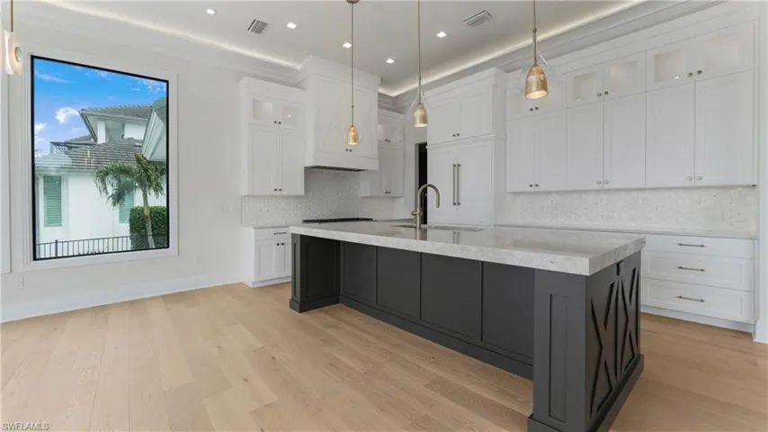 Kitchen with glass insert cabinets, white cabinets, a kitchen island with sink, tasteful backsplash, and light wood finished floors