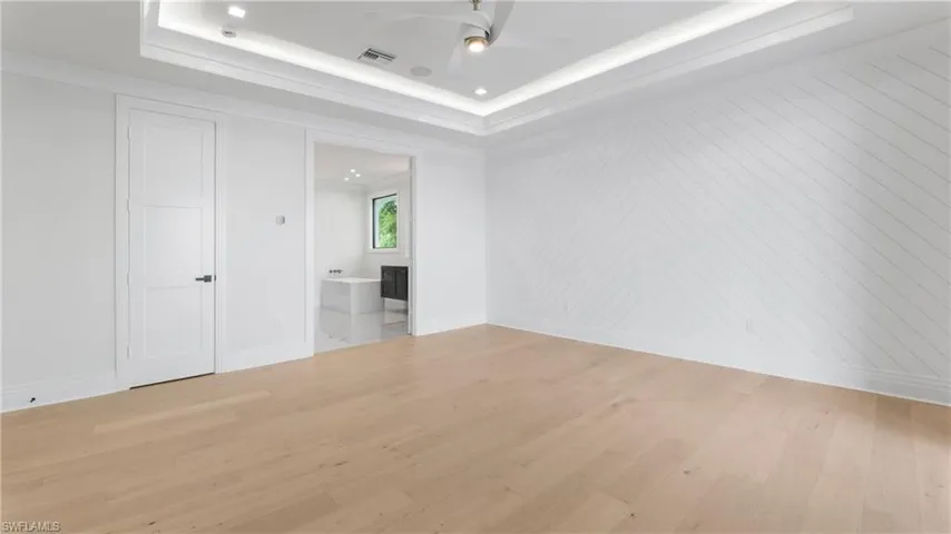 Unfurnished bedroom featuring light wood-type flooring, ensuite bath, a tray ceiling, ceiling fan, and recessed lighting