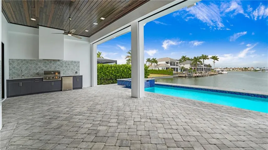 View of swimming pool featuring a patio, ceiling fan, an outdoor kitchen, a pool with connected hot tub, and a residential view