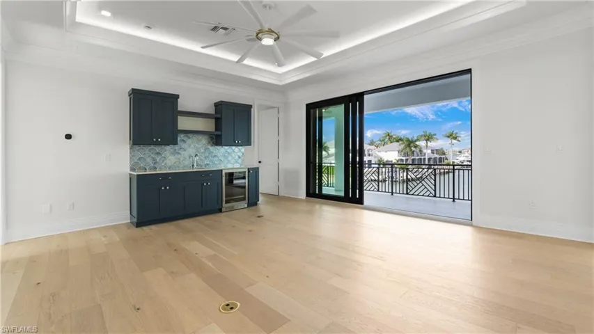 Kitchen with a raised ceiling, tasteful backsplash, light wood finished floors, wine cooler, and ornamental molding