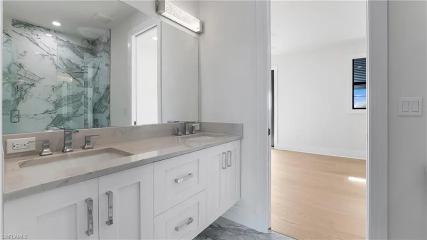 Bathroom with double vanity, a marble finish shower, and light marble finish floors