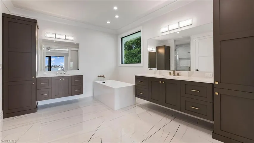 Full bathroom with two vanities, healthy amount of natural light, a shower stall, ornamental molding, and recessed lighting