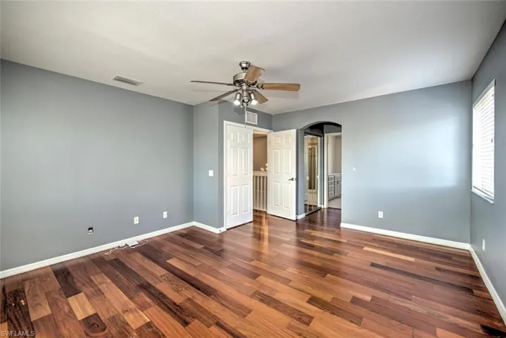 Unfurnished bedroom featuring arched walkways, visible vents, baseboards, and wood finished floors