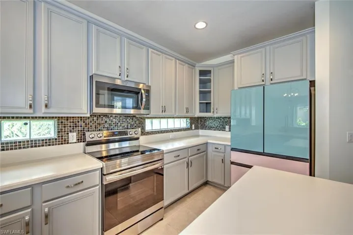 Kitchen with light tile patterned floors, stainless steel appliances, gray cabinets, backsplash, and glass insert cabinets