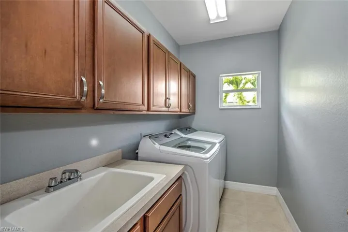 Washroom featuring light tile patterned floors, a sink, baseboards, washer and dryer, and cabinet space