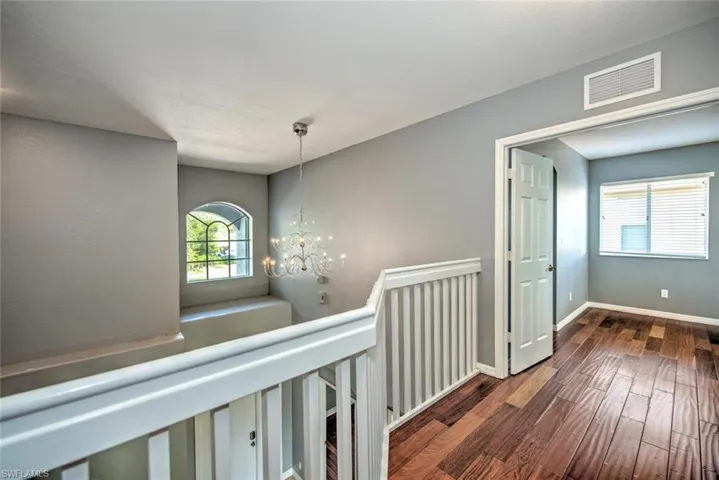 Hallway featuring baseboards, visible vents, wood finished floors, an upstairs landing, and a chandelier
