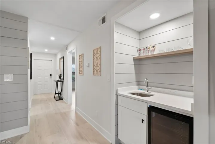 Bar with white cabinets, light hardwood / wood-style floors, wine cooler, and sink