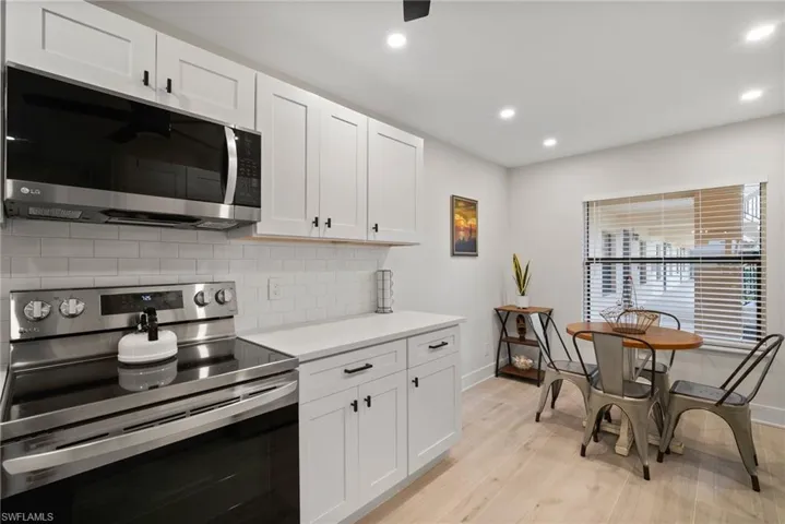 Kitchen with light wood-type flooring, appliances with stainless steel finishes, decorative backsplash, and white cabinets