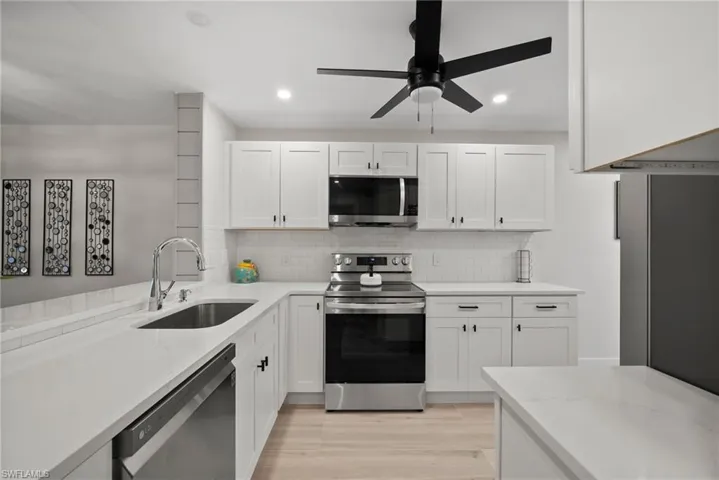 Kitchen with white cabinetry, appliances with stainless steel finishes, light wood-type flooring, decorative backsplash, and sink