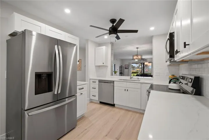 Kitchen featuring stainless steel appliances, white cabinetry, tasteful backsplash, light hardwood / wood-style flooring, and pendant lighting