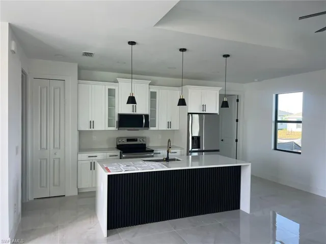 Kitchen with sink, white cabinetry, stainless steel appliances, and a kitchen island with sink