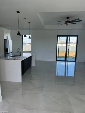 Kitchen with white cabinetry, sink, a large island, hanging light fixtures, and stainless steel refrigerator with ice dispenser
