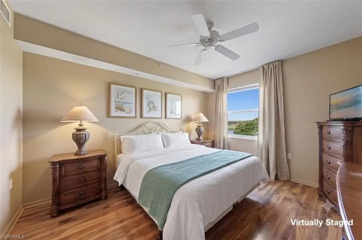 Bedroom featuring wood-finish flooring, a ceiling fan, and a window offering a distant water and tree-lined landscape