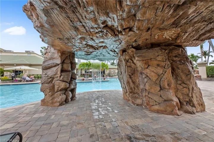 Expansive pool area featuring a rock grotto with cascading water, surrounding paver patio, and mature palm trees