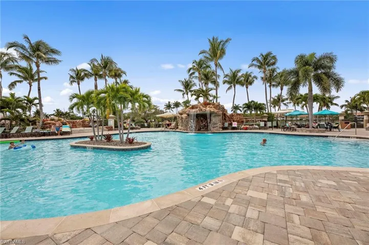 Expansive resort-style pool featuring a rock waterfall, surrounded by mature palm trees