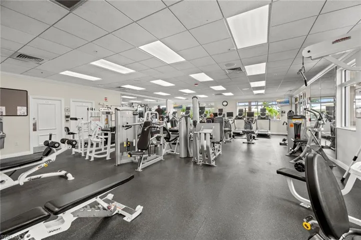 Spacious fitness center featuring various exercise equipment, resilient rubber flooring, drop ceiling with integrated lighting, mirrored wall panels, and large windows along one wall