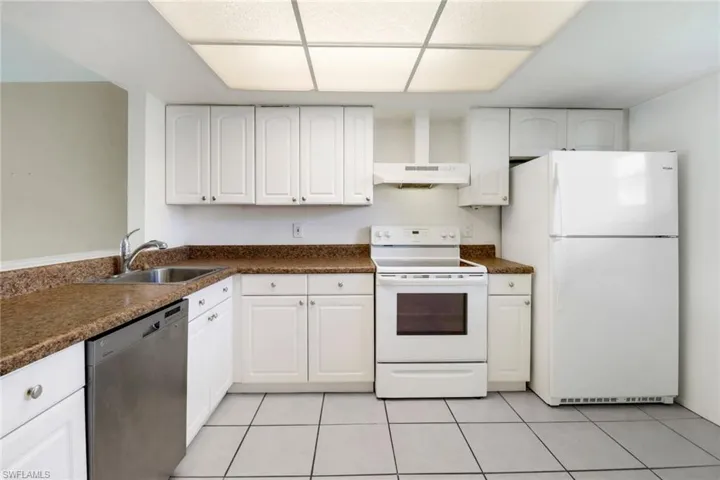 Kitchen featuring white appliances, white cabinets, sink, light tile patterned floors, and wall chimney exhaust hood