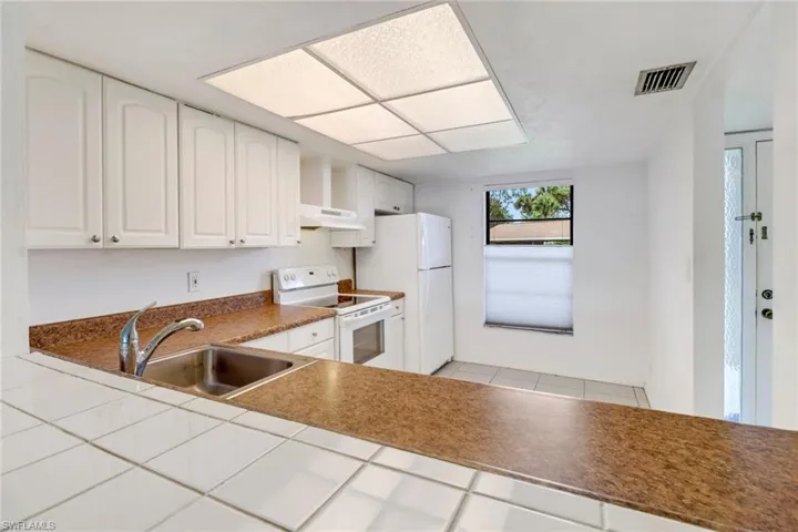 Kitchen featuring light tile patterned flooring, white appliances, white cabinets, wall chimney exhaust hood, and sink