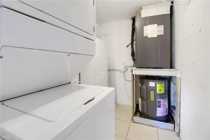 Clothes washing area with stacked washer and clothes dryer, light tile patterned floors, and water heater