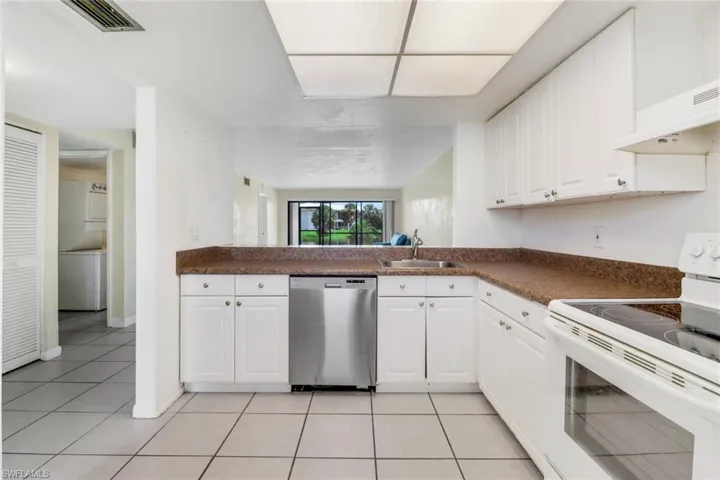 Kitchen featuring light tile patterned flooring, electric range, white cabinets, dishwasher, and sink
