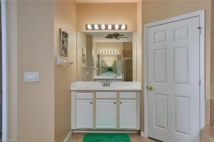 Full bath with ceiling fan, vanity, tile patterned floors, and tiled shower