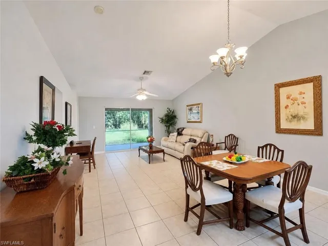 Vaulted ceilings with a decorative chandelier and ceiling fan, neutral tile flooring, and sliding glass doors providing access to the outdoors