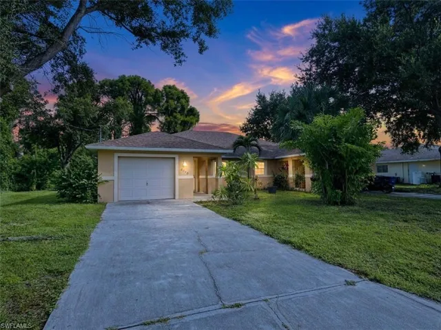Single-story residence featuring a garage, a concrete driveway, and a front yard with mature trees
