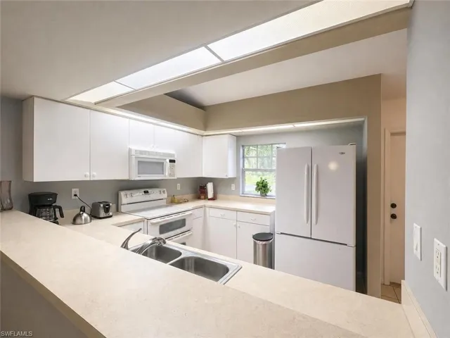 Kitchen with white cabinetry, light-toned countertops, a double basin sink, and a built-in microwave