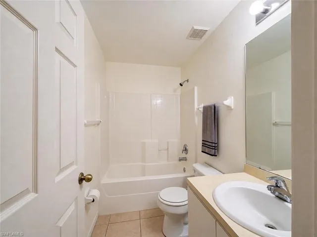 Bathroom featuring a tub and shower combination with tile surround, a single vanity with an integrated sink, a large wall-mounted mirror, and tile flooring