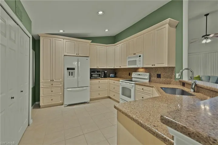 Kitchen with decorative backsplash, sink, light tile patterned floors, white appliances, and ceiling fan