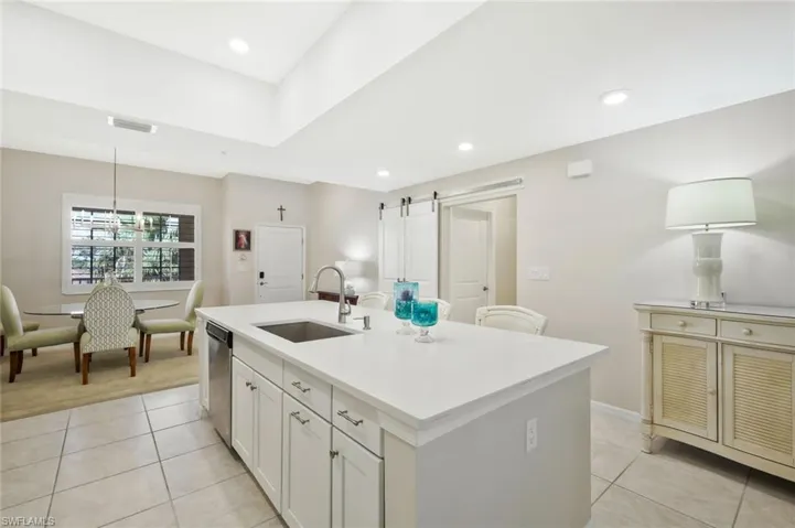 Kitchen featuring a barn door, a center island with sink, light tile patterned flooring, and white cabinetry
