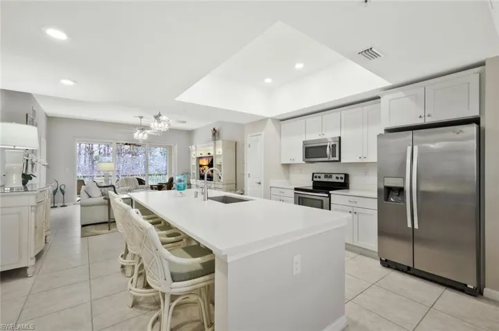 Kitchen with stainless steel appliances, a kitchen bar, white cabinets, a kitchen island with sink, and light tile patterned floors