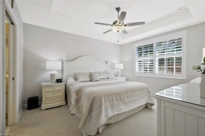 Bedroom with ceiling fan, a tray ceiling, and light colored carpet