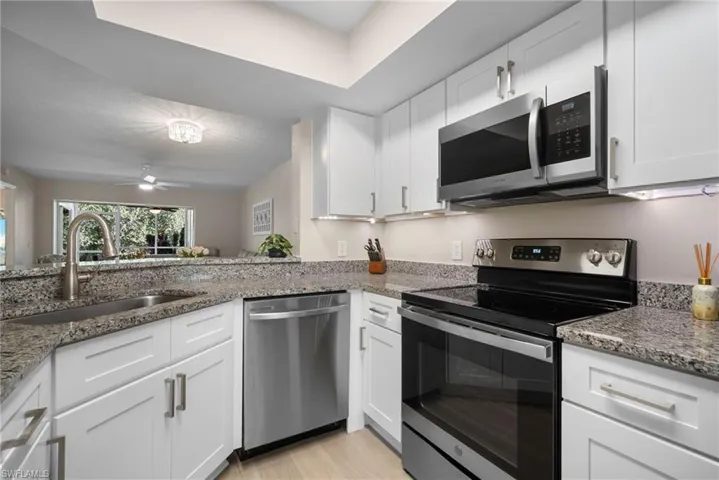 Kitchen with appliances with stainless steel finishes, white cabinets, and light stone countertops