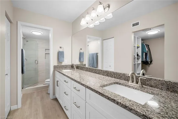 Full bath with double vanity, a shower stall, light wood-type flooring, and a spacious closet