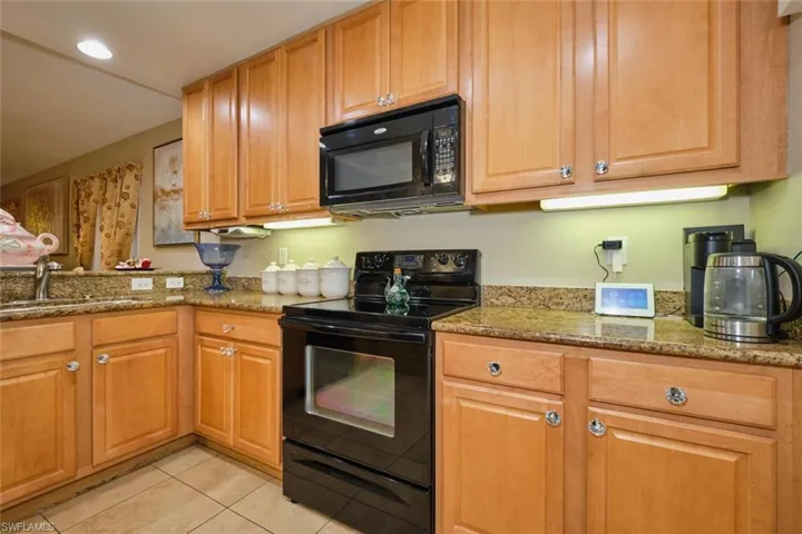 Kitchen featuring black appliances, stone counters, sink, and light tile patterned floors