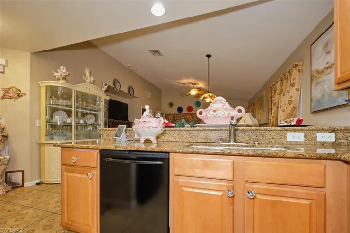 Kitchen featuring black dishwasher, sink, pendant lighting, light tile patterned floors, and light stone countertops